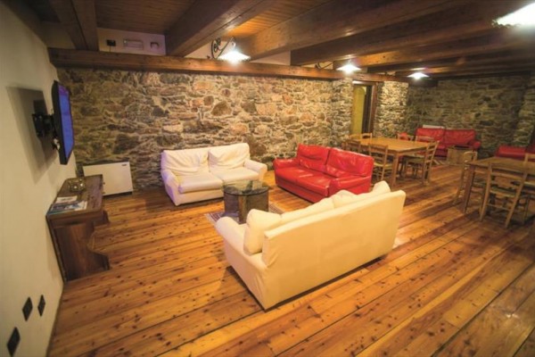 Przytulny salon z kamiennymi ścianami, drewnianą podłogą i sofami w jasnych i czerwonych odcieniach.