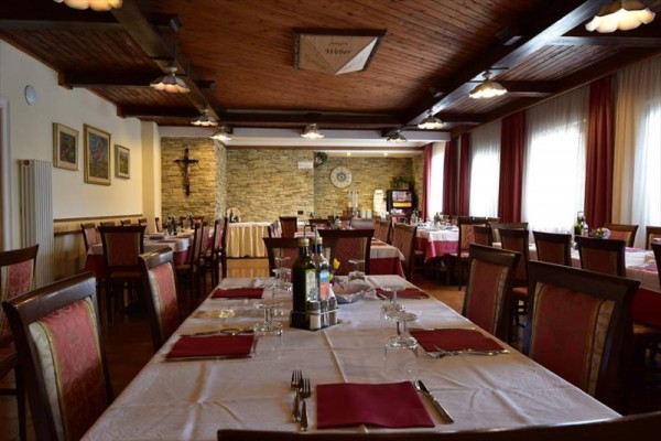 Restauracja z drewnianym sufitem i przygotowanymi stołami z czerwonymi obrusami.