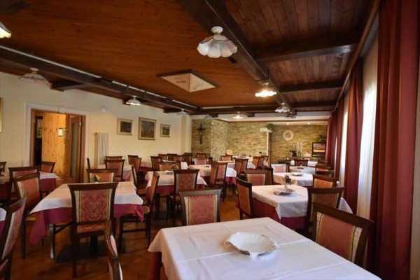 Restauracja z drewnianym sufitem, nakrytymi stołami i czerwonymi zasłonami.