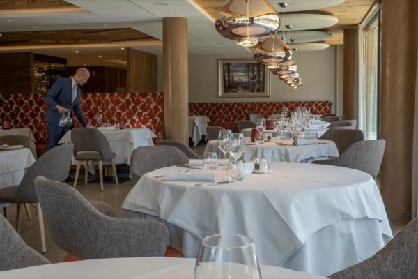 Luksusowa restauracja z okrągłymi stołami i przygotowanym nakryciem, mężczyzna nalewa wodę.