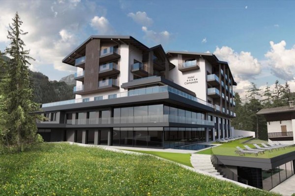 Nowoczesny górski hotel z przeszkloną fasadą otoczony lasami i łąką.