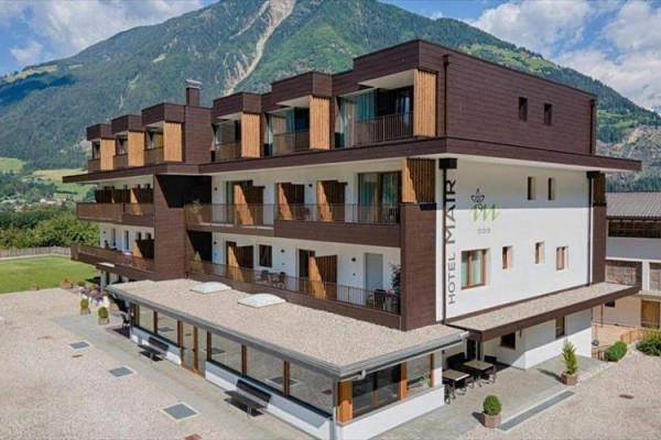 Nowoczesny hotel z drewnianymi balkonami na tle masywu górskiego.