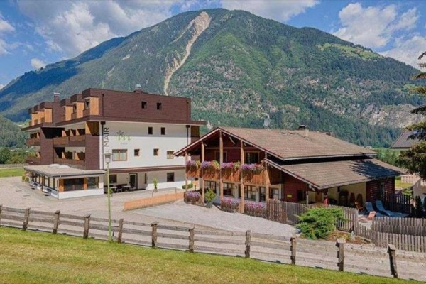 Górski hotel z drewnianymi balkonami pełnymi kwiatów u podnóża zielonej góry.