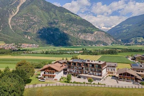 Hotel otoczony zielonymi polami i górami na horyzoncie pod niebieskim niebem z chmurami.