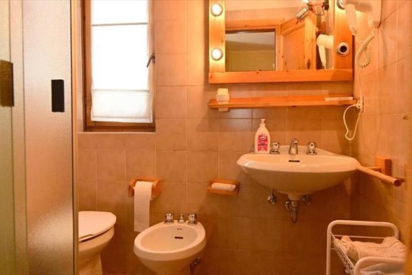 Łazienka z prysznicem, umywalką, lustrem, bidetem i WC w ciepłych odcieniach.