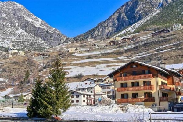 Alpejska wioska z drewnianymi domami na zboczu ośnieżonej góry pod niebieskim niebem.