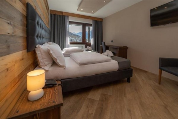 Nowoczesny pokój hotelowy z podwójnym łóżkiem, drewnianą okładziną i oknem z widokiem na góry.