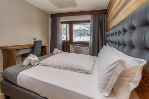 Pokój hotelowy z łóżkiem małżeńskim i oknem z widokiem na ośnieżone góry.