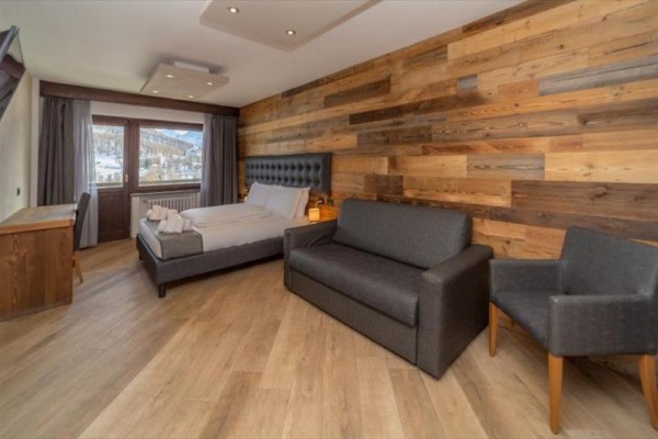 Nowoczesny pokój hotelowy z drewnianą ścianą, łóżkiem małżeńskim i sofą.