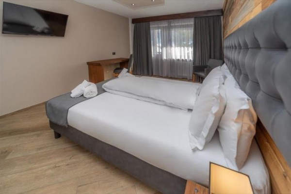 Nowoczesny pokój hotelowy z dużym łóżkiem, biurkiem i telewizorem na ścianie.