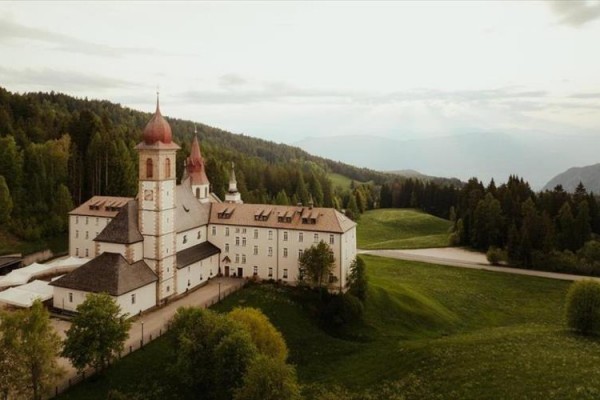 Klasztor otoczony zielonymi łąkami i lasami w górskim krajobrazie.  