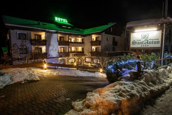 Nocny widok na oświetlony hotel z zaśnieżonym krajobrazem i napisem Hotel Sant Anton.