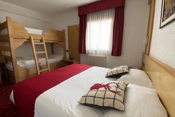 Pokój hotelowy z łóżkiem małżeńskim i łóżkiem piętrowym, czerwone akcenty.