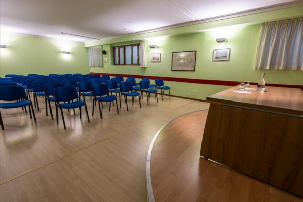 Pusta sala wykładowa z niebieskimi krzesłami i mównicą.