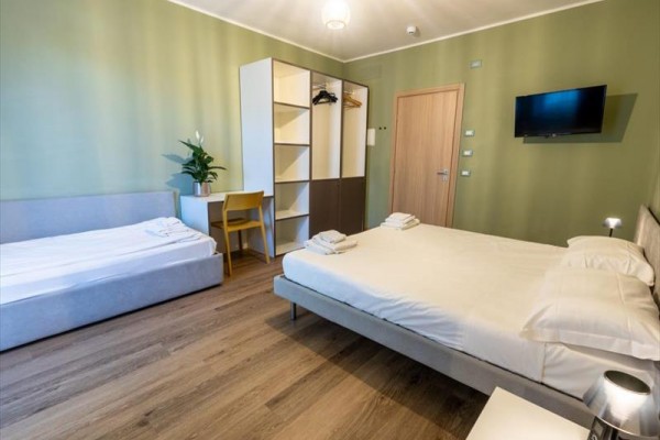 Nowoczesny pokój hotelowy z łóżkiem małżeńskim, pojedynczym łóżkiem, szafą i telewizorem na ścianie.