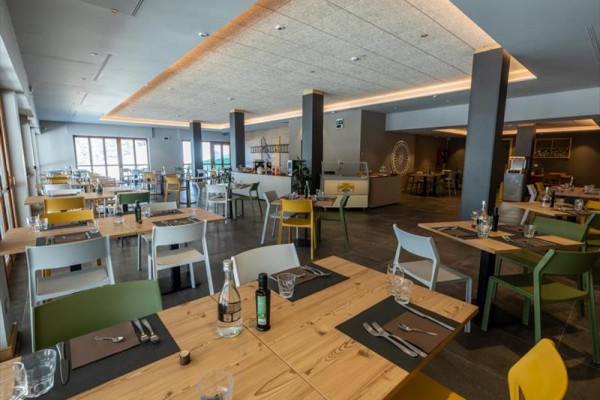 Nowoczesna restauracja z drewnianymi stołami, kolorowymi krzesłami i minimalistycznym oświetleniem.