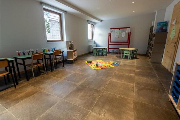 Sala zabaw z dziecięcymi stołami, krzesłami i zabawkami na podłodze.