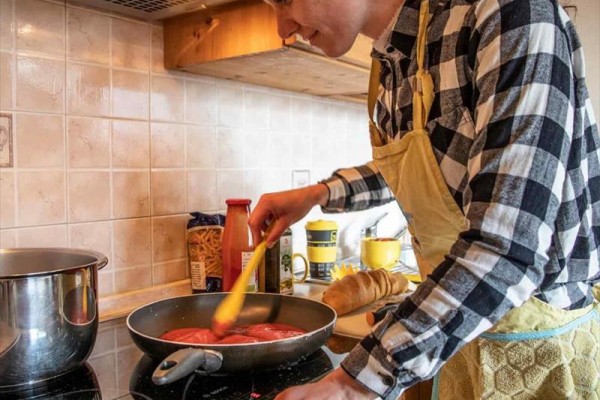 Osoba mieszająca sos pomidorowy na patelni w kuchni.