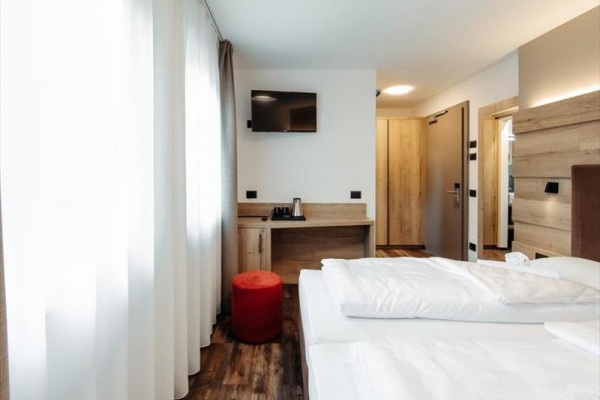 Jasny pokój hotelowy z łóżkiem małżeńskim, telewizorem na ścianie i biurkiem.