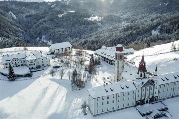 Pokryty śniegiem klasztor otoczony lasami w zimowym krajobrazie.