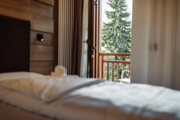 Z otwartego okna sypialni widać balkon i drzewa na zewnątrz.