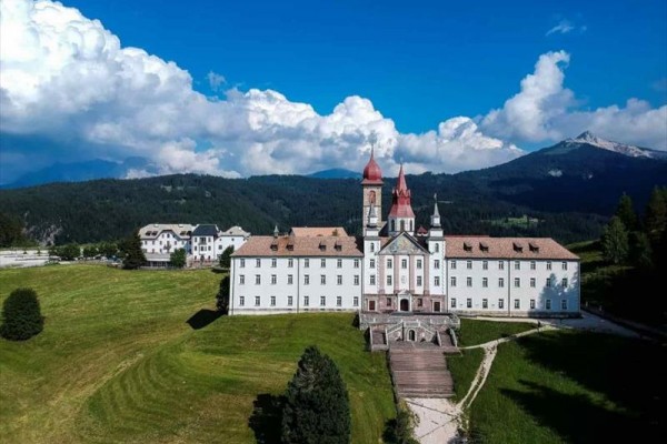 Historyczny budynek z wieżami na tle gór i niebieskiego nieba z chmurami.