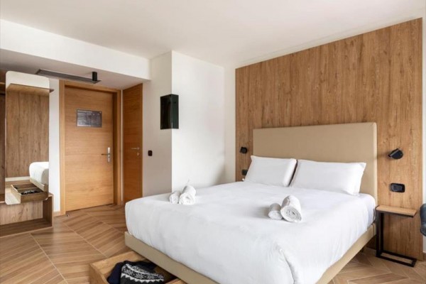 Nowocześnie urządzony pokój hotelowy z łóżkiem małżeńskim i drewnianymi elementami.