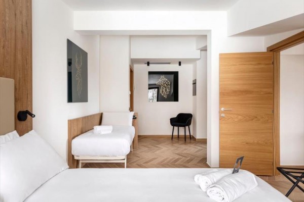 Nowoczesny, jasny pokój hotelowy z podwójnym łóżkiem, oddzielnym łóżkiem i otwartymi drzwiami.