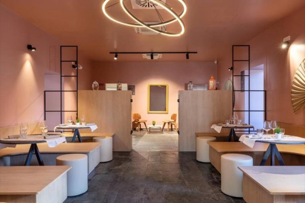Nowoczesna restauracja z różowymi ścianami, okrągłymi stołami i drewnianymi ławkami.