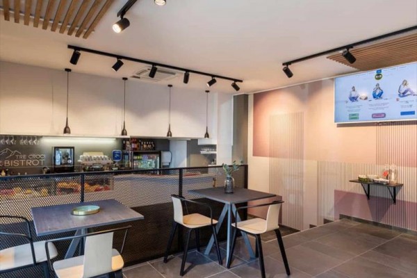 Nowoczesna kawiarnia z prostymi meblami, wiszącymi lampami i dużym obrazem na ścianie.