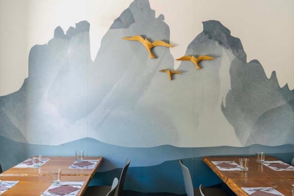 Drewniane ptaki lecące na tle malowidła ściennego z motywem gór w stylowym wnętrzu restauracji.