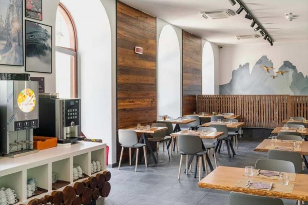 Nowoczesna restauracja z drewnianymi stołami i ścianami, ozdobiona obrazami i malowidłem ściennym gór.