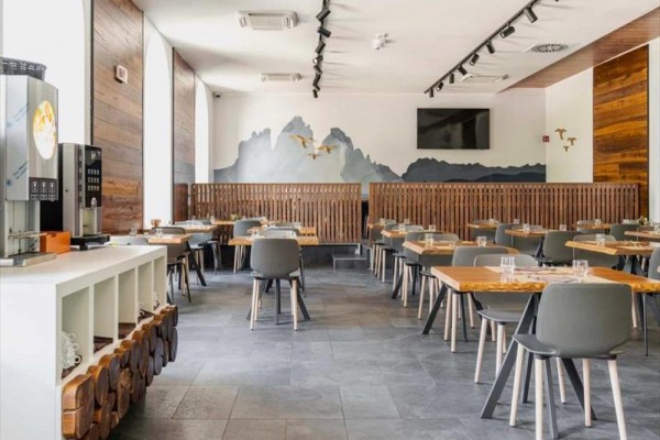 Nowoczesna restauracja z drewnianymi meblami i muralem górskim na ścianie.