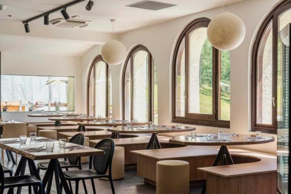 Restauracja z drewnianymi meblami i oknami łukowymi z widokiem na przyrodę.