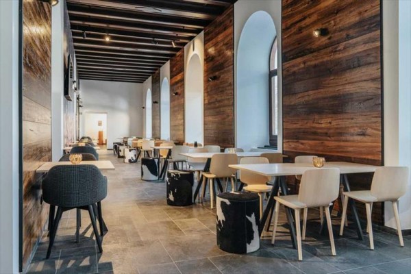Nowoczesna kawiarnia z drewnianymi panelami, białymi stołami i designerskimi krzesłami.