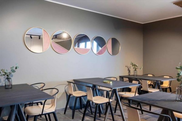 Nowoczesna kawiarnia z czterema stolikami, schludnie ustawionymi krzesłami i lustrami na ścianie.