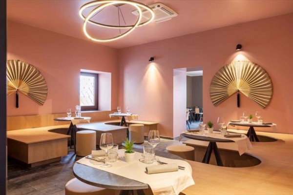 Nowoczesna restauracja z okrągłymi stołami, różowymi ścianami i dekoracyjnymi wachlarzami.