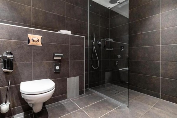 Nowoczesna łazienka z toaletą, prysznicem i ciemnymi kafelkami.