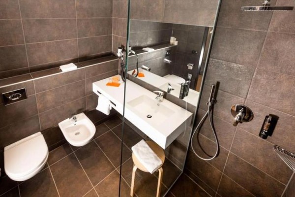 Nowoczesna łazienka z ciemnymi płytkami, prysznicem, umywalką i toaletą.