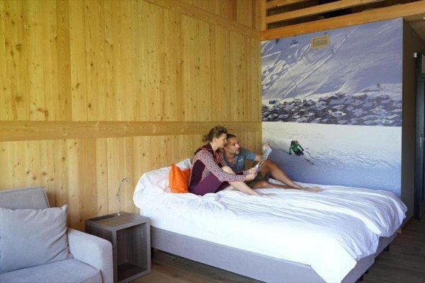 Para siedzi na łóżku w drewnianym pokoju z obrazem narciarza na ścianie.