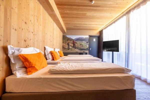 Pokój z drewnianą boazerią, trzema łóżkami z pomarańczowymi poduszkami i dużymi oknami.