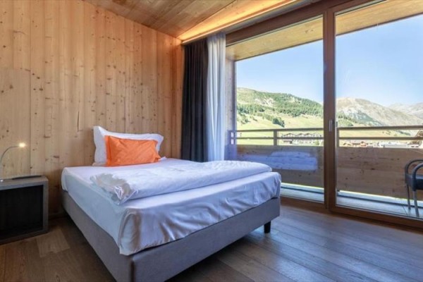 Nowoczesna sypialnia z pojedynczym łóżkiem przy dużym oknie z widokiem na góry.