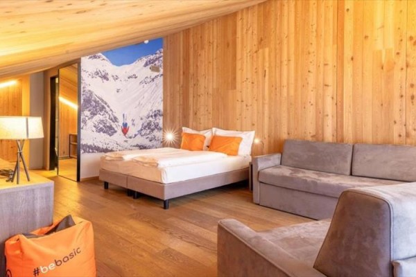 Pokój z drewnianymi ścianami, łóżkiem, sofą i lampą, z obrazem gór na ścianie.