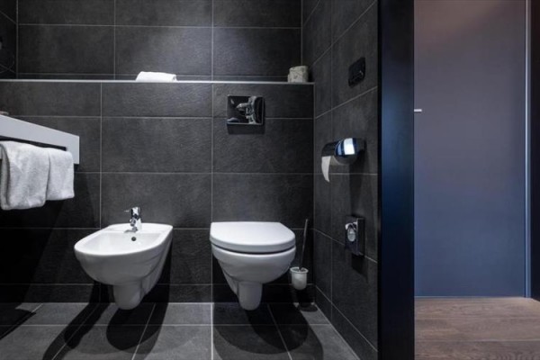Nowoczesna łazienka z bidetem i toaletą na czarnych kafelkach.