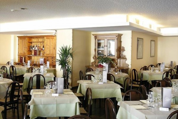 Restauracja ze stolikami pokrytymi białymi obrusami i zielonymi nakryciami, gotowa do obsługi.