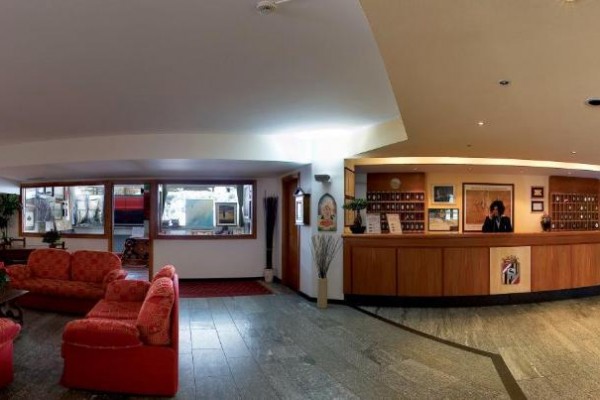 Recepcja hotelowa z czerwonymi sofami i ladą recepcyjną po prawej stronie.
