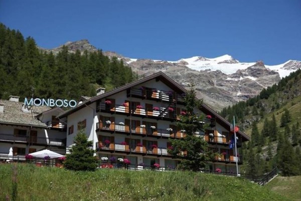 Górski hotel z balkonami ozdobionymi kwiatami, otoczony lasami i górami.