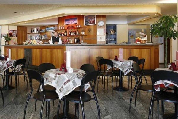 Bar z drewnianym blatem i stołami z obrusami, wokół których stoi kilka krzeseł.
