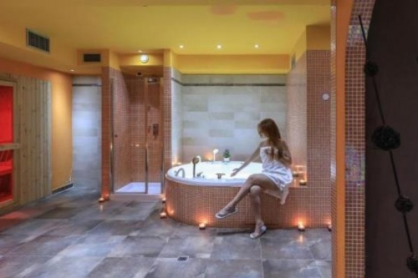 Pomieszczenie wellness z jacuzzi i sauną na podczerwień, gdzie siedzi kobieta w białym ręczniku.
