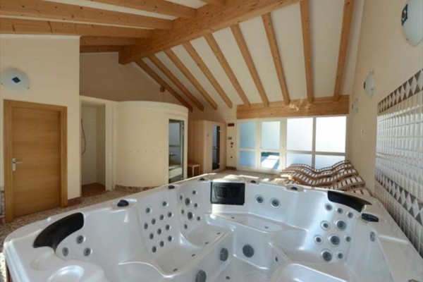 Nowoczesne pomieszczenie z jacuzzi i leżakami pod drewnianym belkowym sufitem.